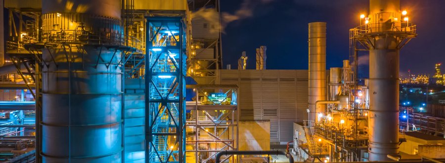 Complexo industrial de energia iluminado à noite, com torres e tubulações